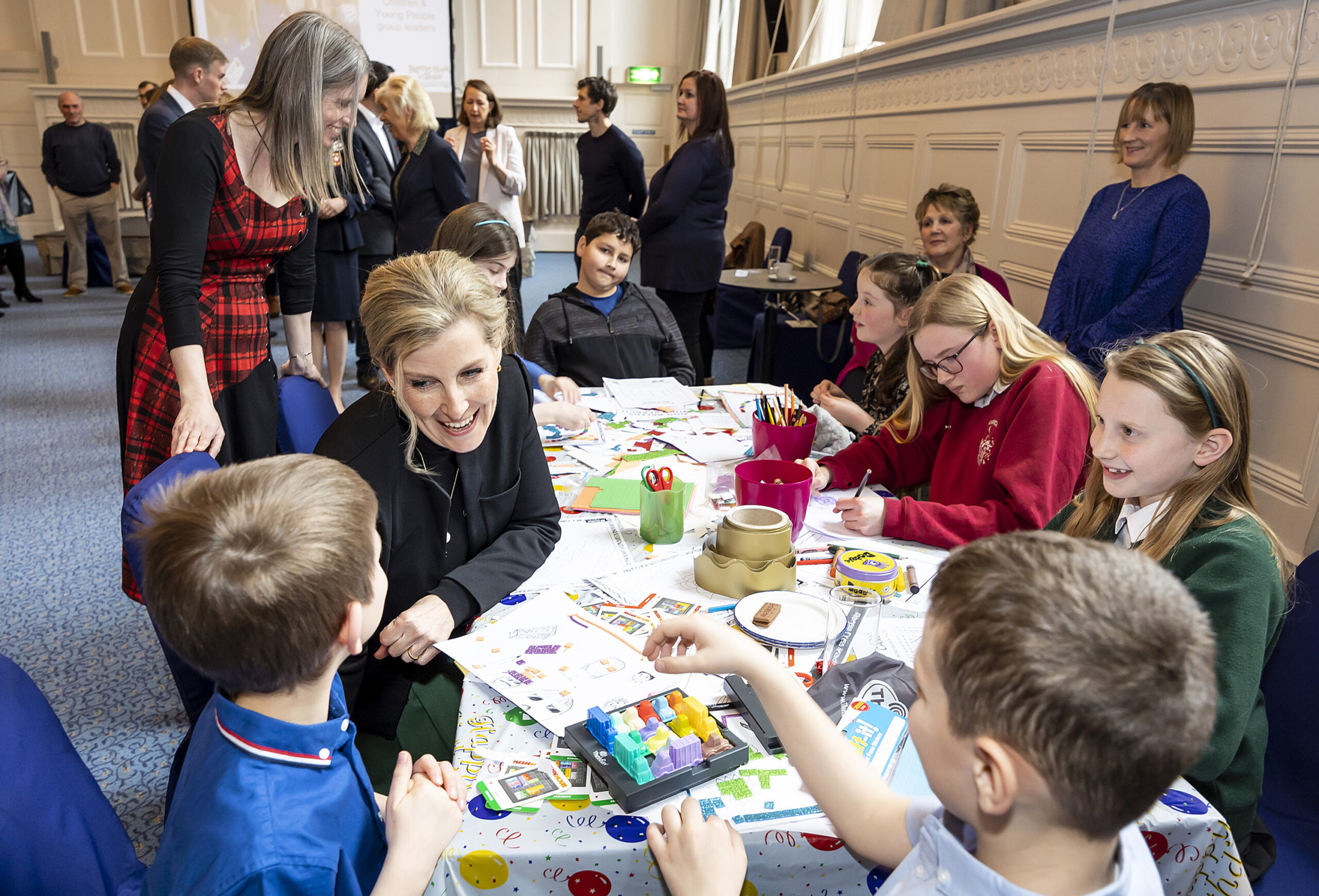 A photograph of HRH The Countess of Wessex surrounded by a group of children doing craft